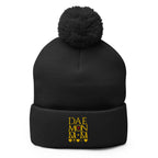 Daemon Luxury Nemesis Sun Glow black pom-pom-knit beanie cap, front view showcasing cozy wool texture and stylish design.