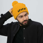 Golden pom-pom knit cap featuring a front logo patch, from Daemon Luxury's Honeybee California G.T. Caped Heroes collection.