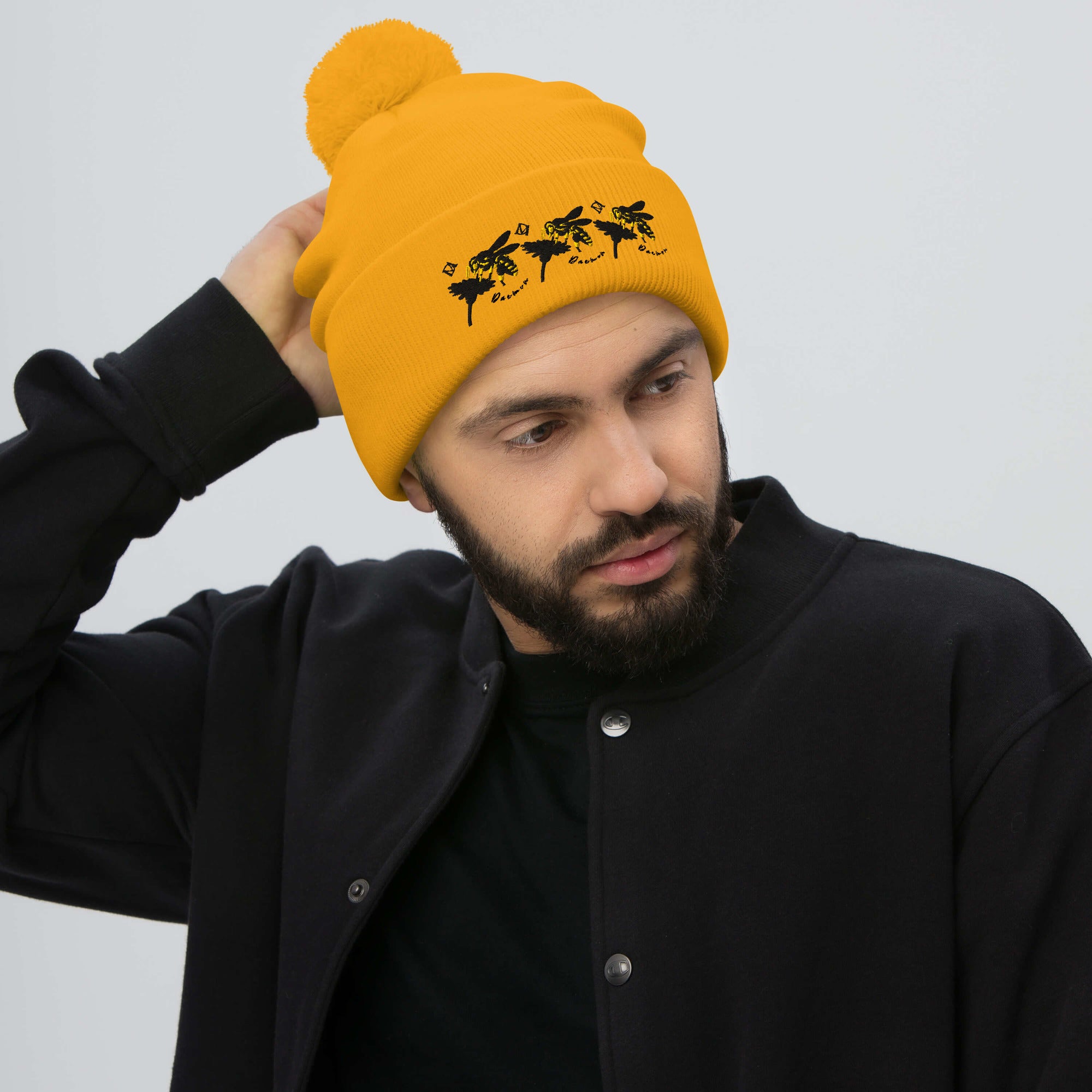 Golden pom-pom knit cap featuring a front logo patch, from Daemon Luxury's Honeybee California G.T. Caped Heroes collection.